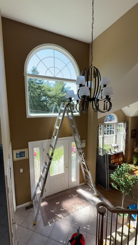 Technician cleaning interior windows near a chandelier